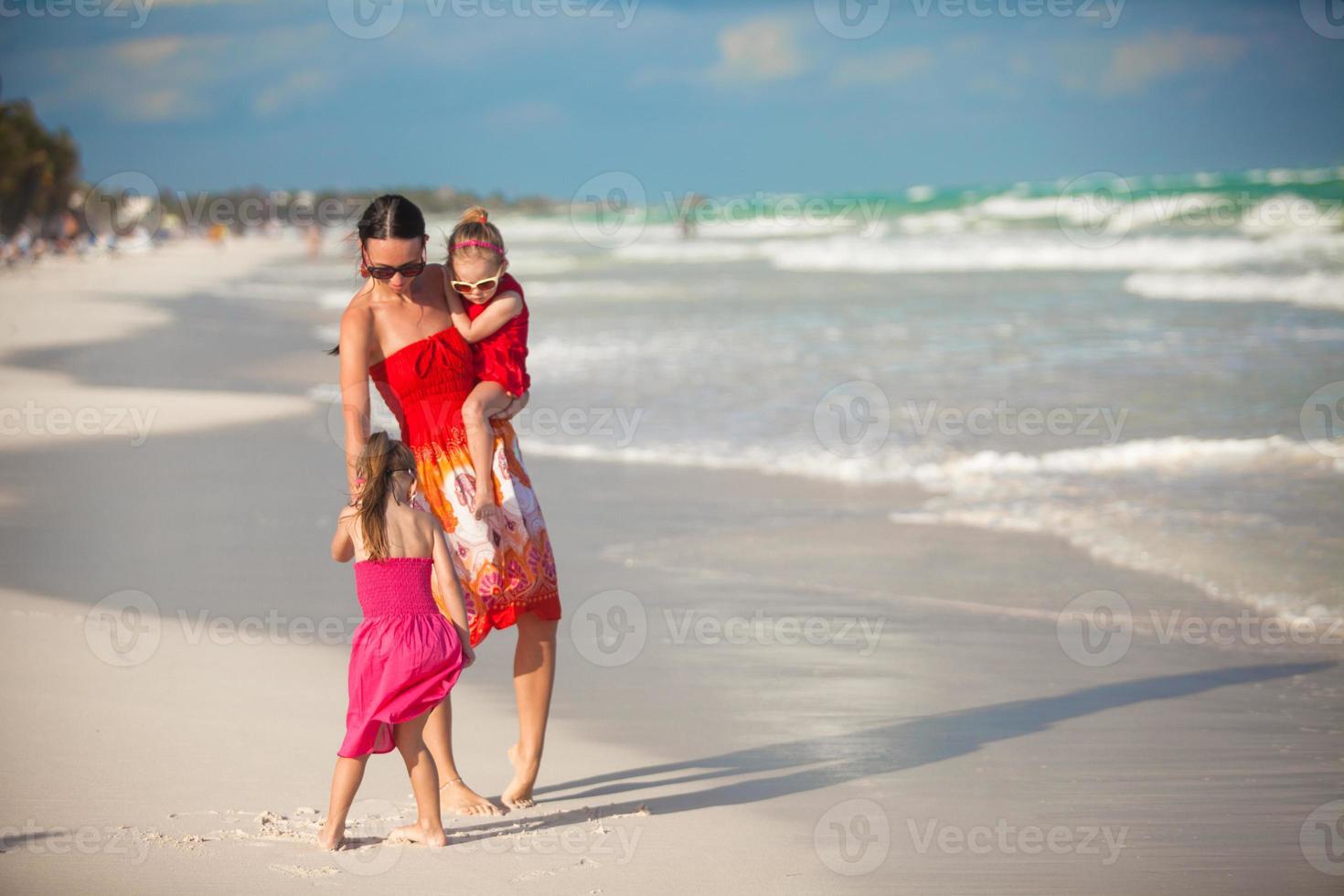 ung mor och två henne mode döttrar gående på exotisk strand på solig dag foto