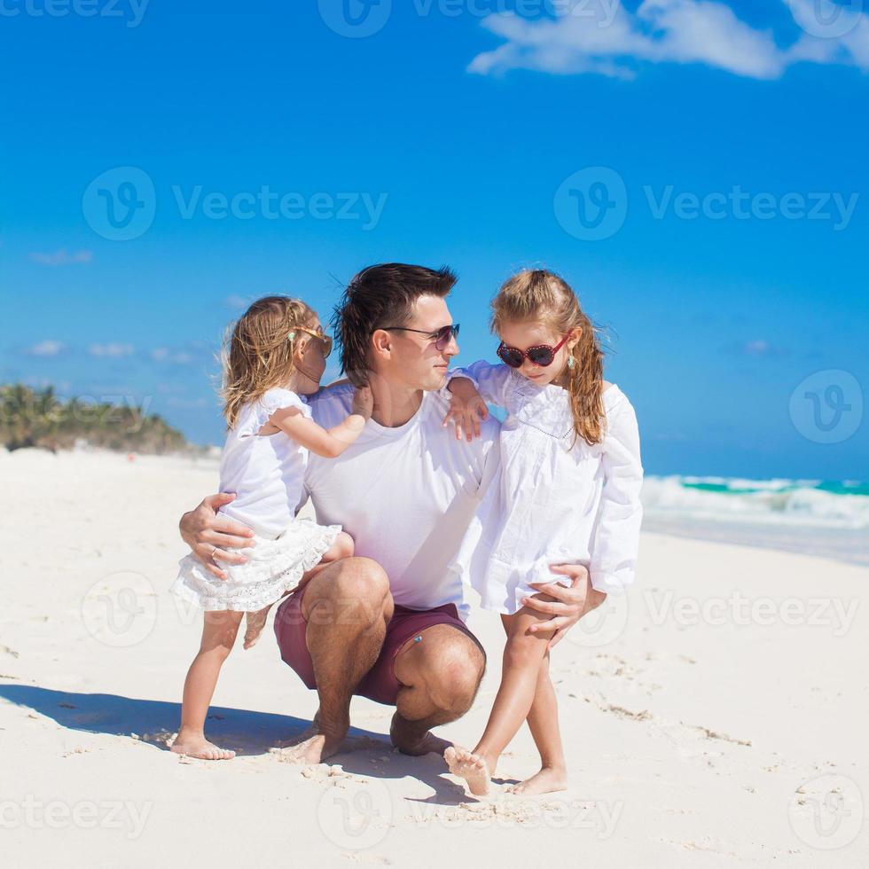 ung Lycklig far och liten döttrar har roligt på vit strand i solig dag foto
