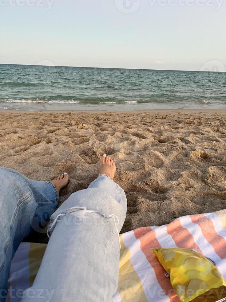 Lycklig kvinna njuter skön solnedgång på de strand. närbild ben på de sand foto