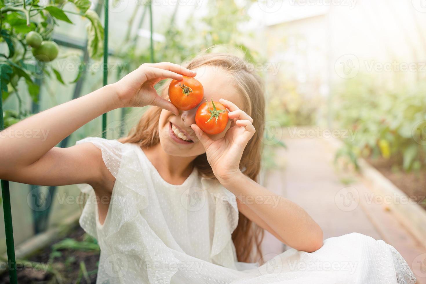 förtjusande flicka har roligt i växthus. porträtt av unge med korg med grönsaker foto