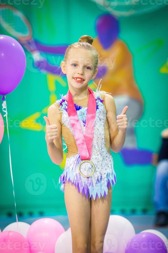 liten charmig gymnast med medalj efter de rytmisk gymnastik konkurrens foto