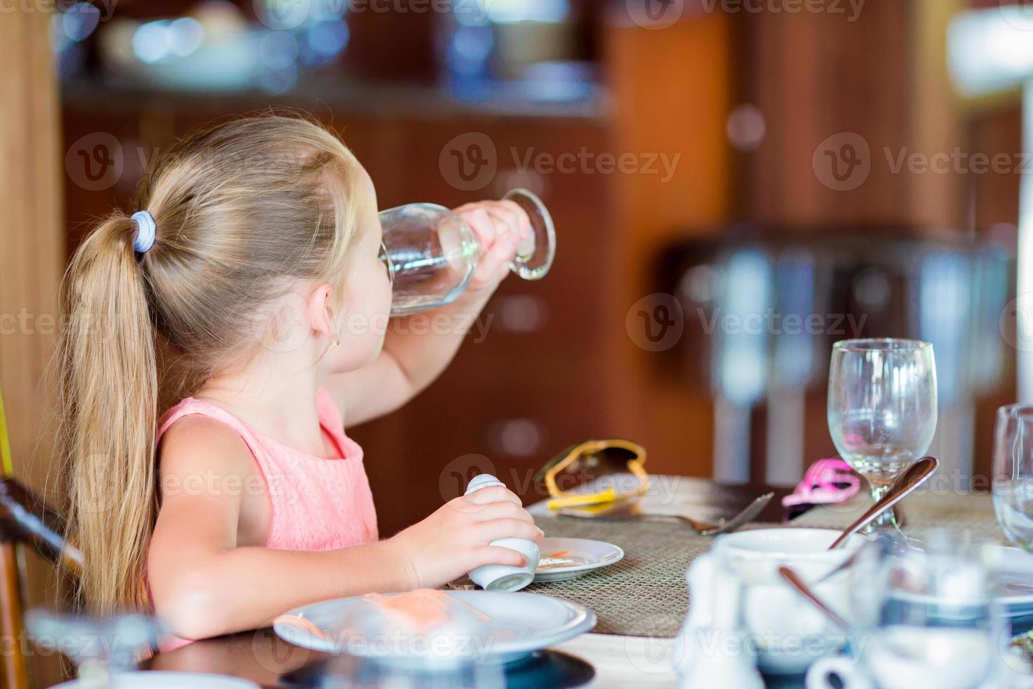 liten flicka ha frukost dricka vatten på utomhus- Kafé foto