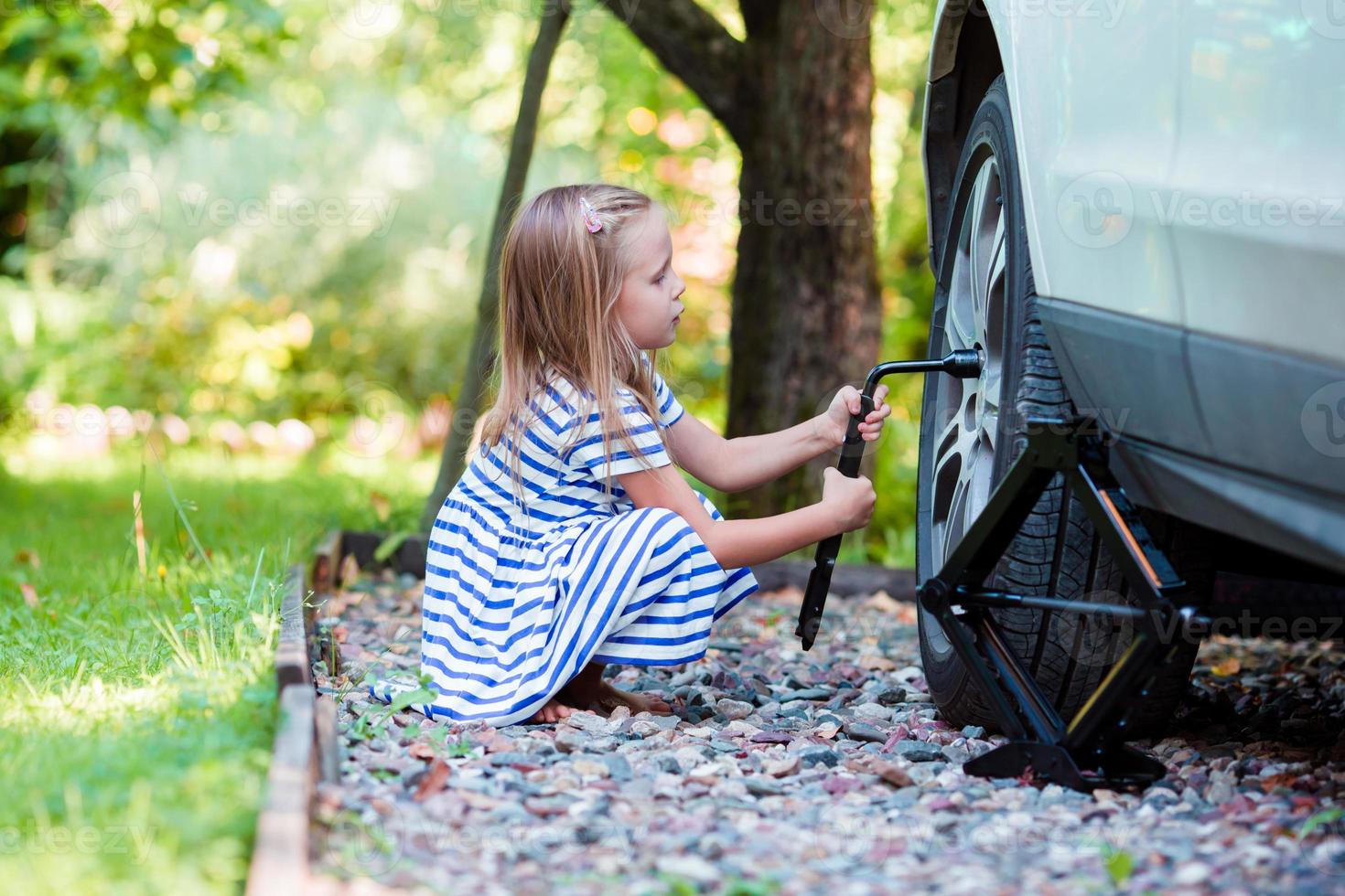 förtjusande liten flicka ändring en bil hjul utomhus på skön sommar dag foto