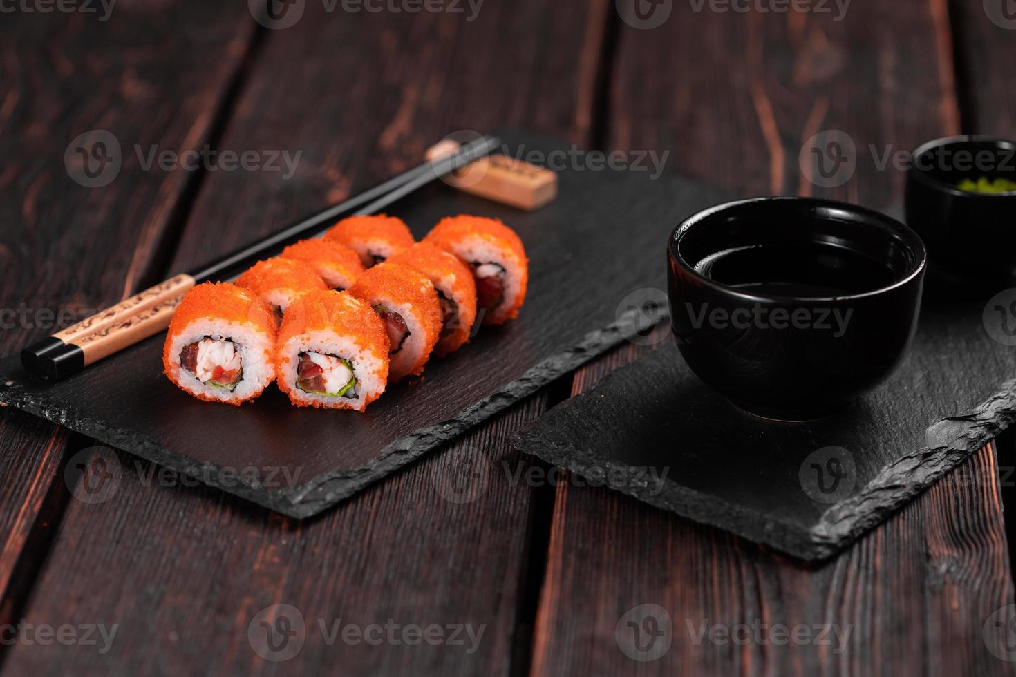 sushi rulla med räka och röd peppar och tobiko kaviar med sallad eras på svart styrelse närbild - japansk mat foto