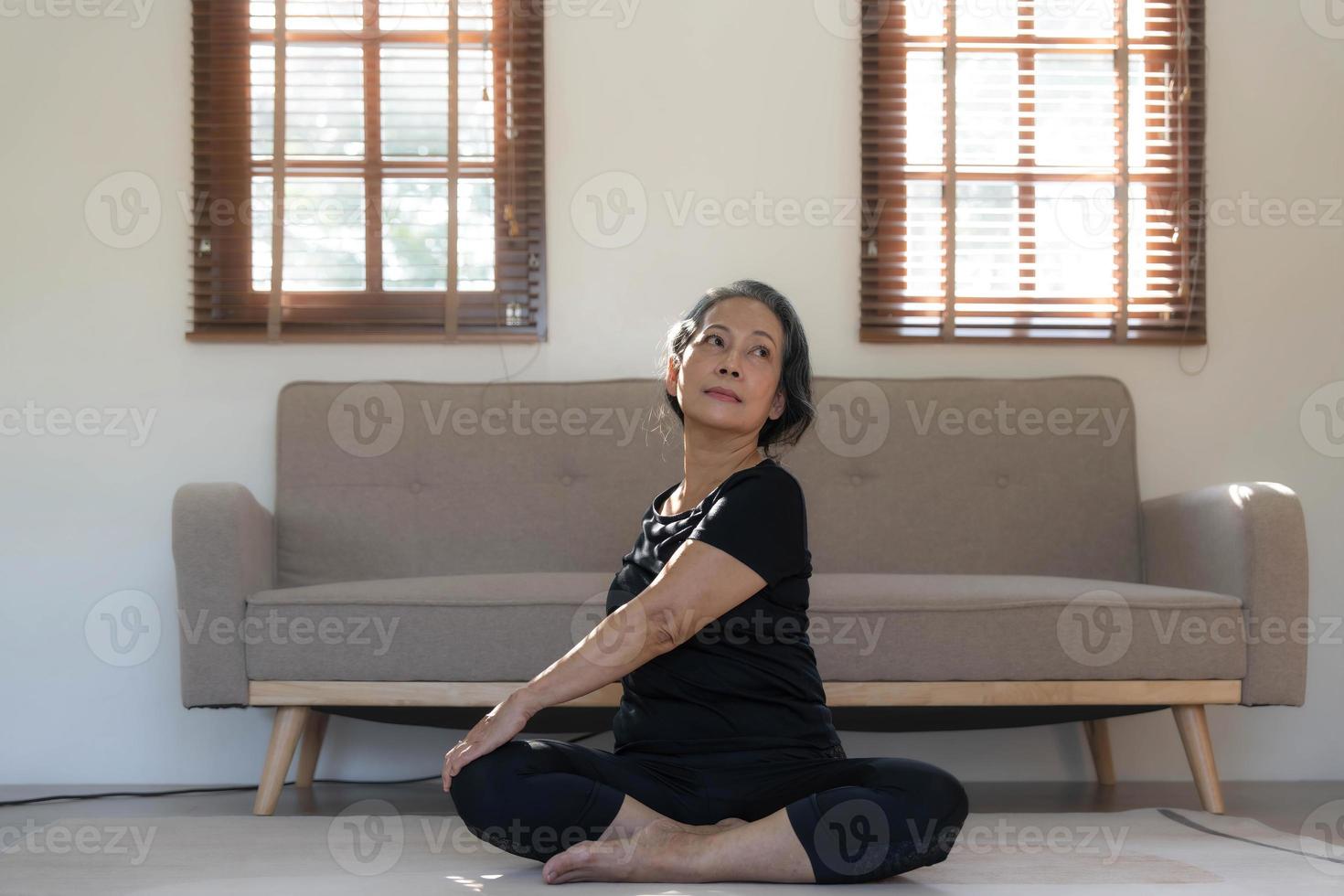 friska och Lycklig 60s pensionerad asiatisk kvinna i träna kläder praktiserande yoga i henne levande rum. foto