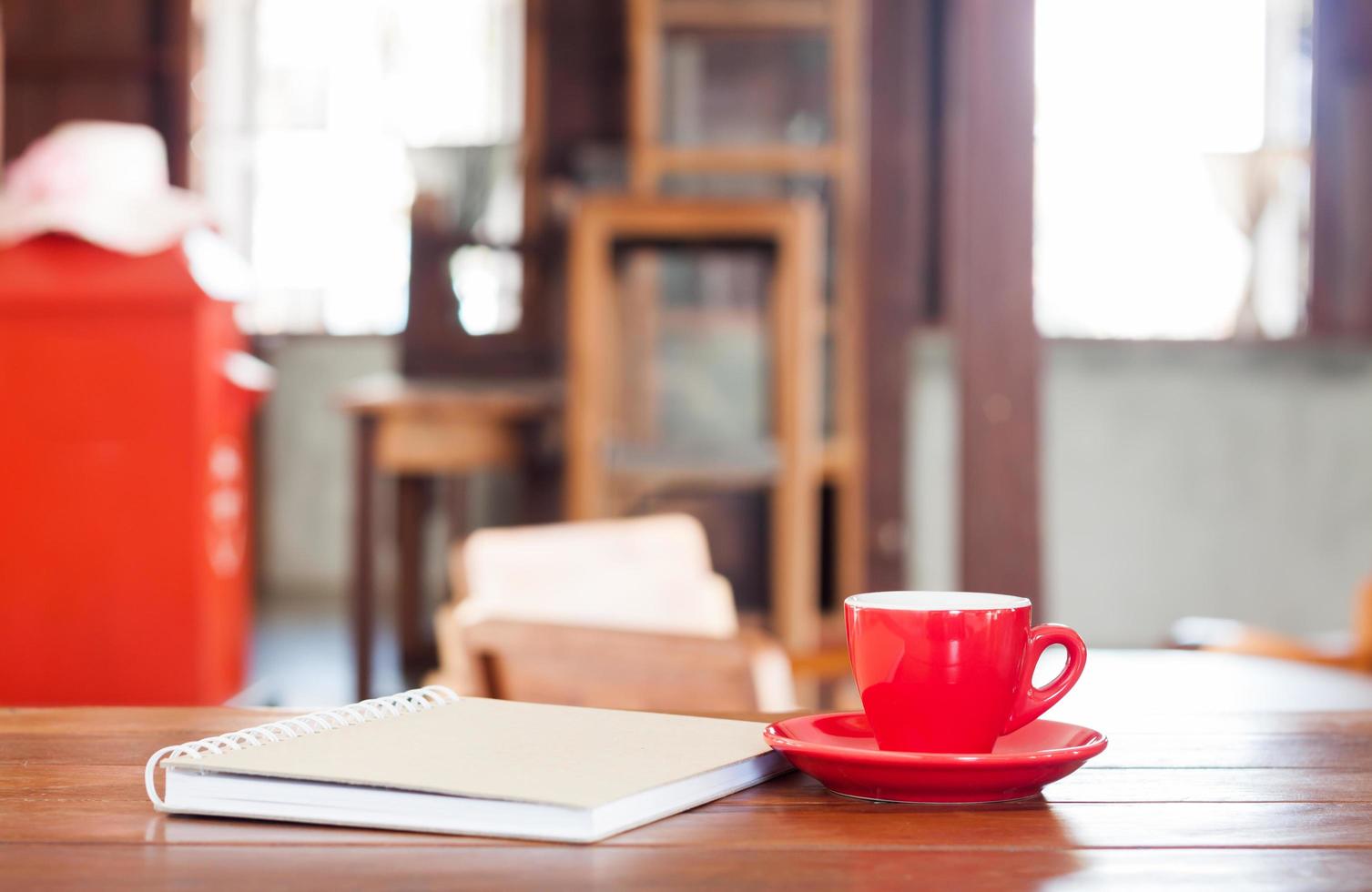 röd kaffekopp med en anteckningsbok på ett träbord foto