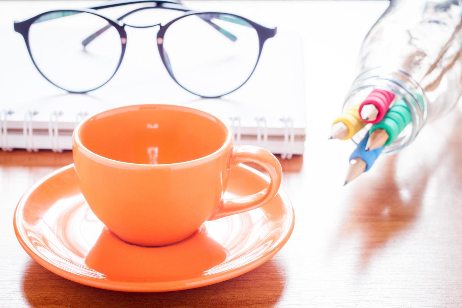 närbild av en kaffekopp med glasögon och pennor foto