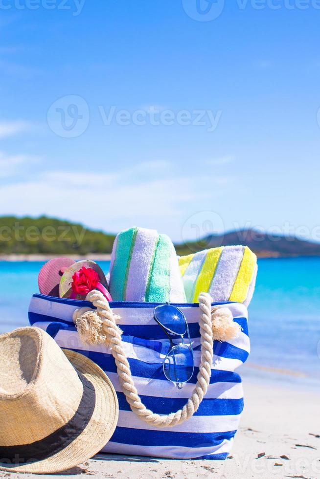 blå väska, stråhatt, flip-flops och handduk på den vita stranden foto