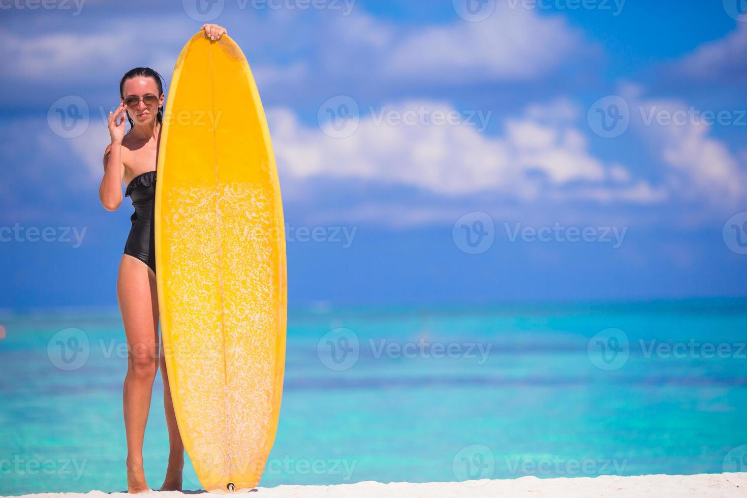 Lycklig smal surfa kvinna på vit strand med gul surfingbräda foto