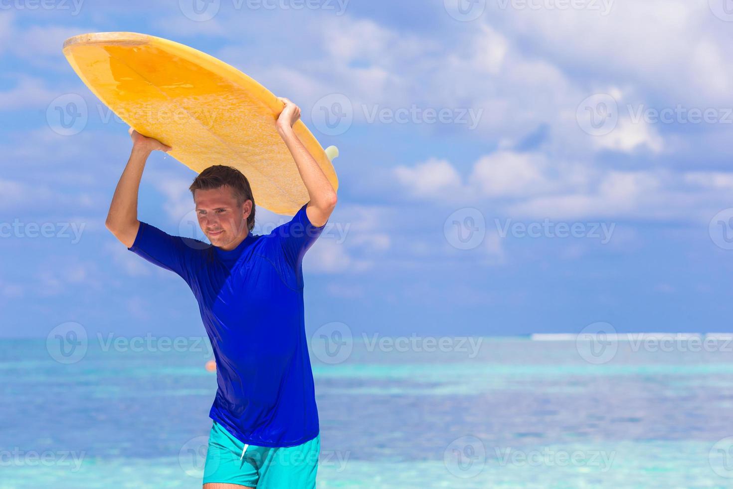 Lycklig ung surfa man på vit strand med gul surfingbräda foto