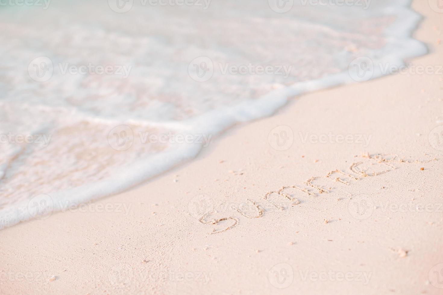 ord sommar handskriven på sandig strand med mjuk hav Vinka på bakgrund foto