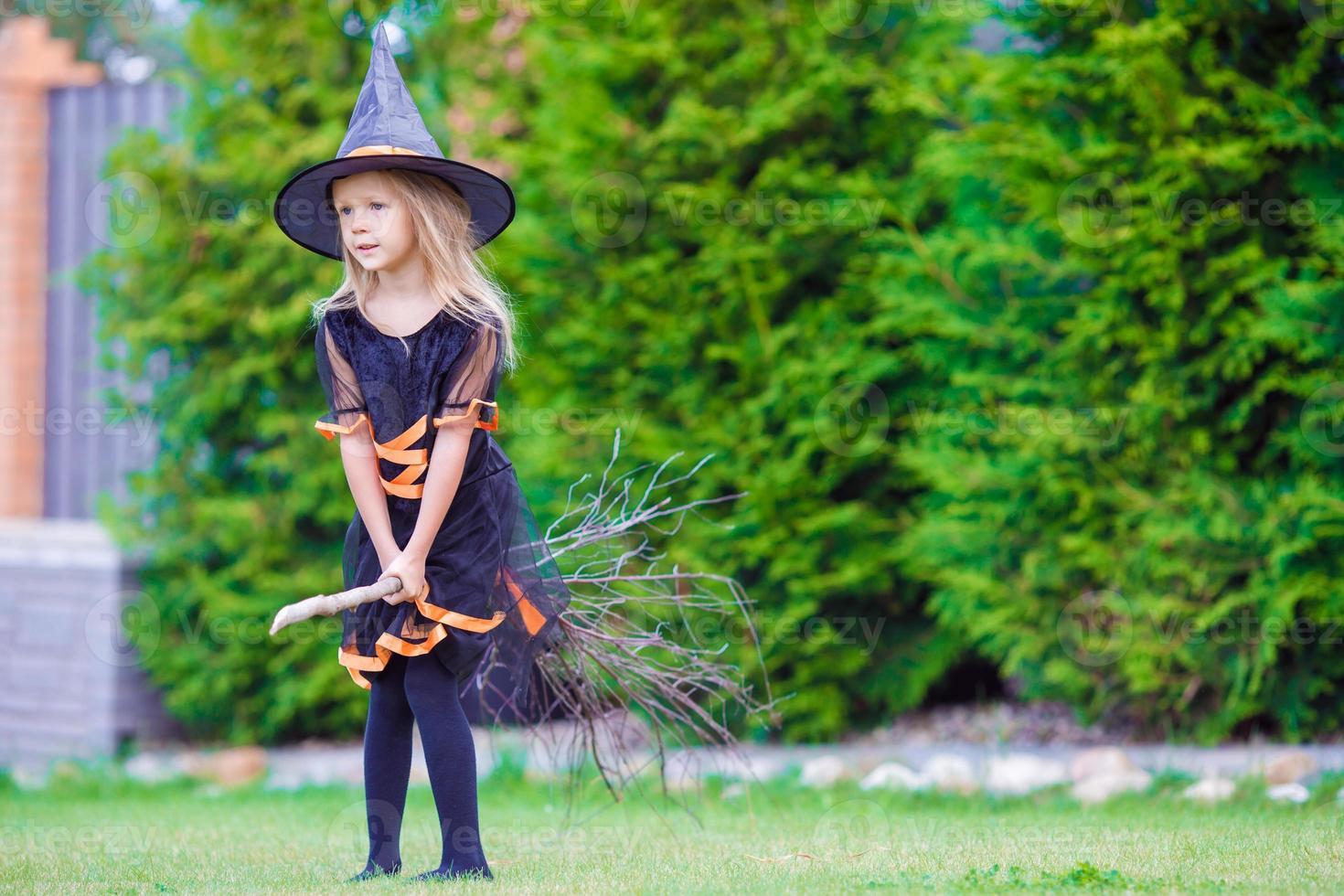 förtjusande liten flicka bär häxa kostym på halloween utomhus. lura eller behandla. foto