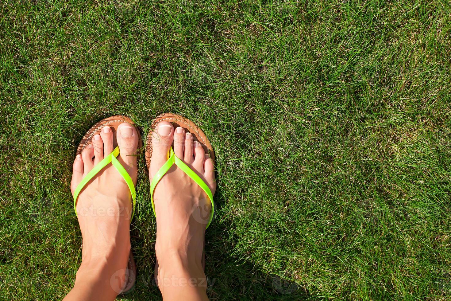 närbild av ljus flip flops och ben på grön gräs foto