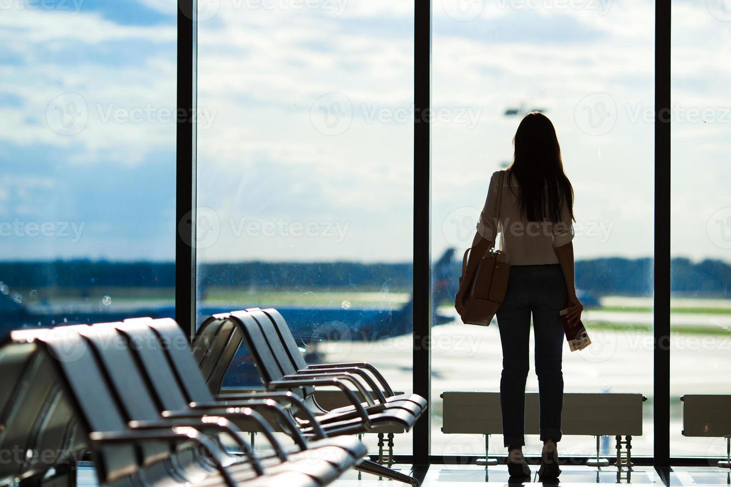 ung kvinna nära fönster i ett flygplats vardagsrum väntar för flyg flygplan foto