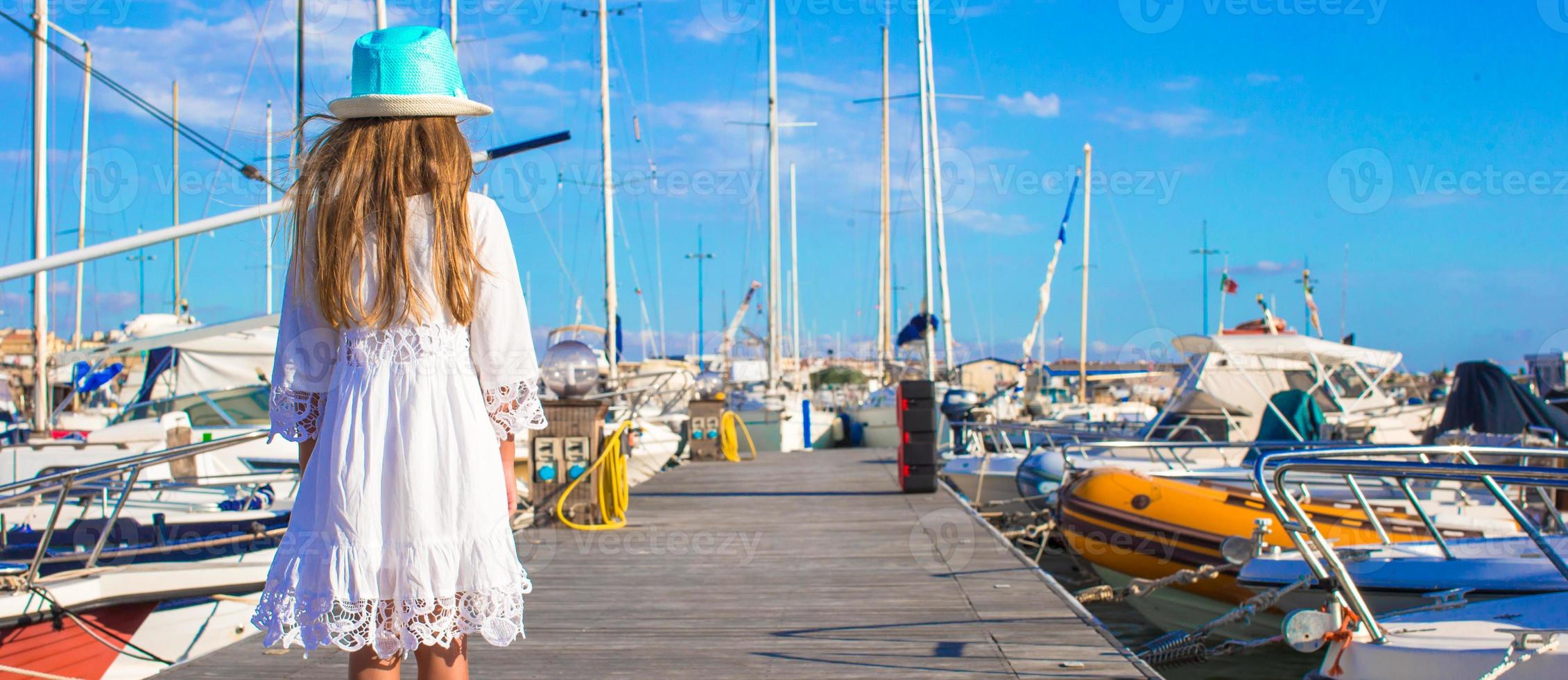 förtjusande liten flicka ha roligt i en hamn på sommar dag foto