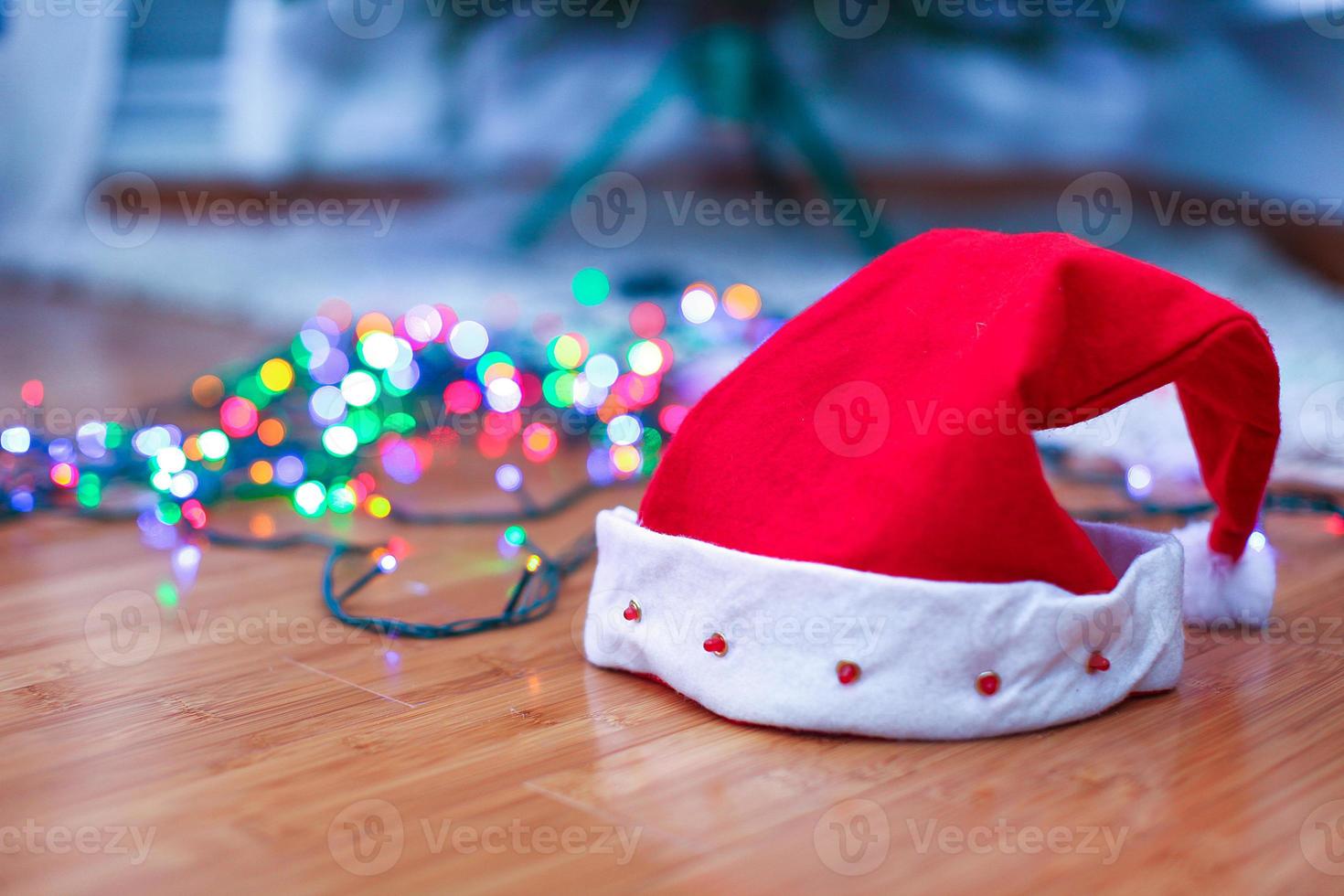 röd santa claus hatt på en timmer golv med ljust färgad girlander, i lampor bakgrund. foto