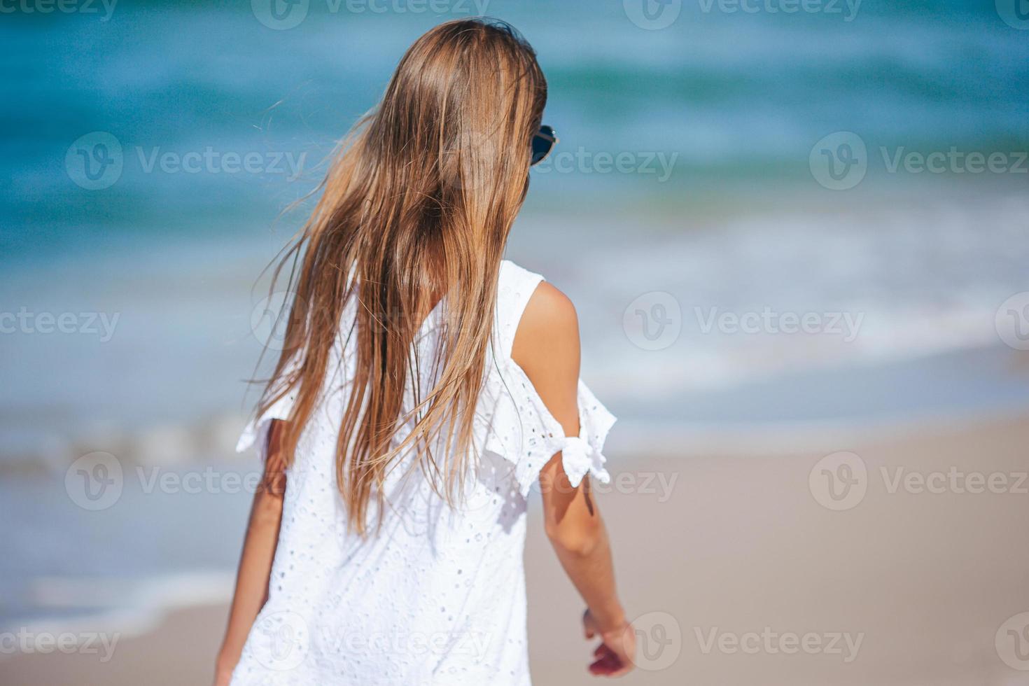 tillbaka se av förtjusande liten flicka med lång hår i vit klänning gående på tropisk strand semester foto