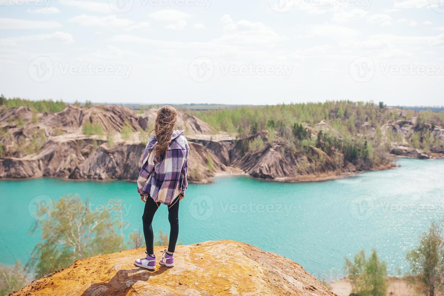 skön flicka på de topp av de sten med blå sjö på bakgrund foto