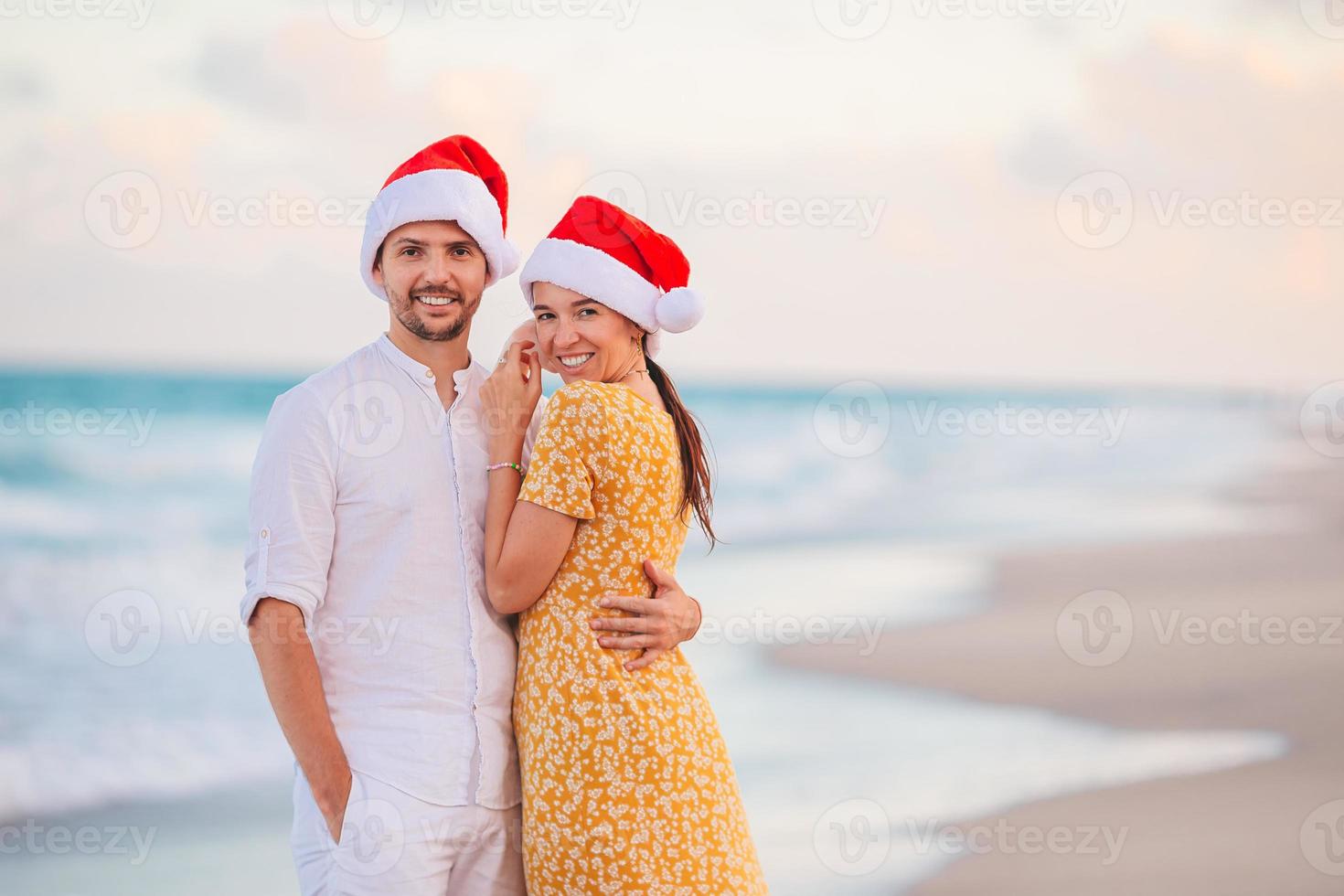 porträtt av jul Lycklig par i santa hattar på strand semester har roligt foto