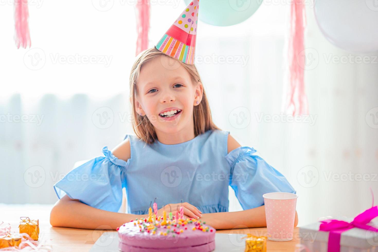 caucasian flicka är drömmande leende och ser på födelsedag regnbåge kaka. festlig färgrik bakgrund med ballonger. födelsedag fest och lyckönskningar begrepp. foto