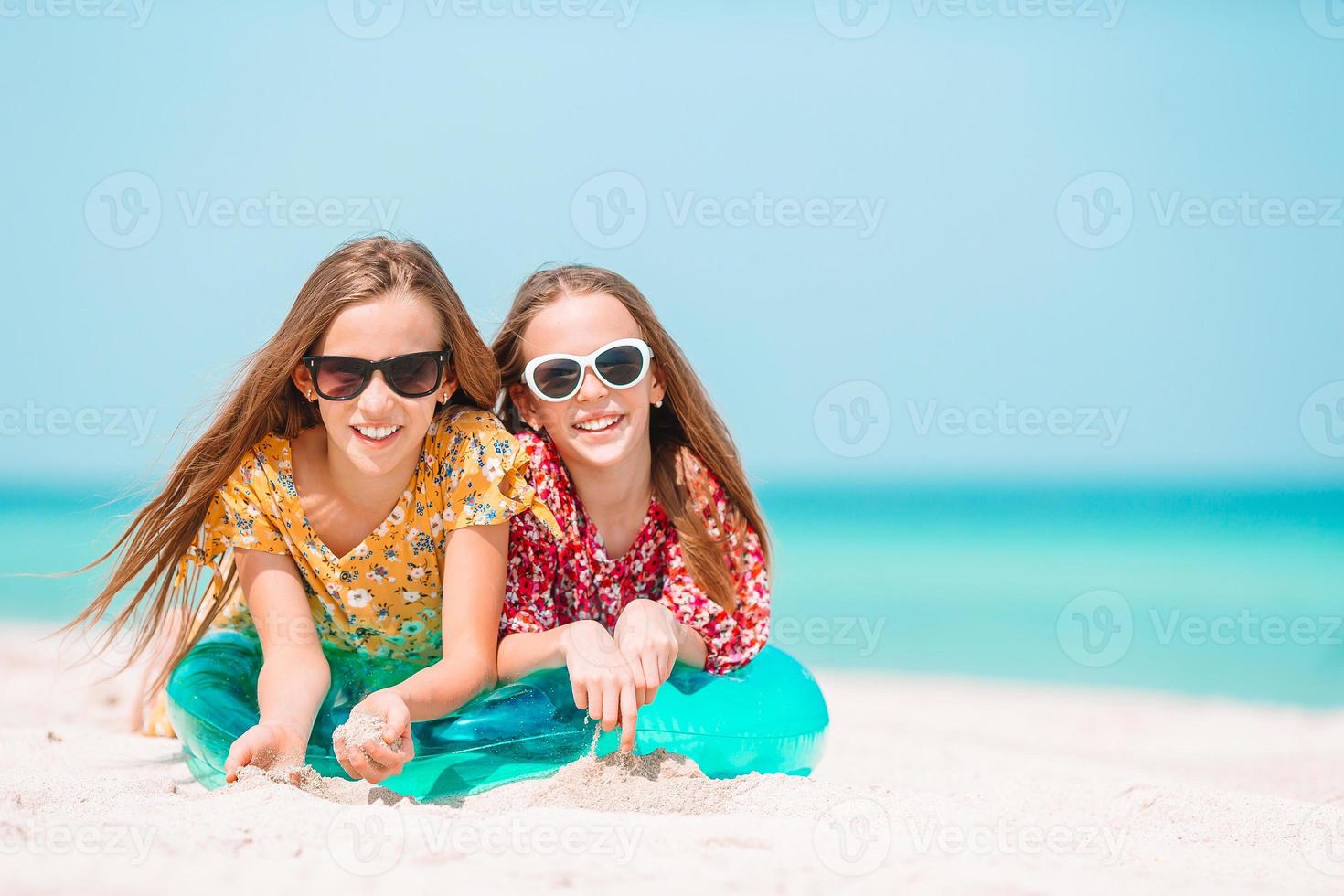 två liten Lycklig flickor ha en massa av roligt på tropisk strand spelar tillsammans foto