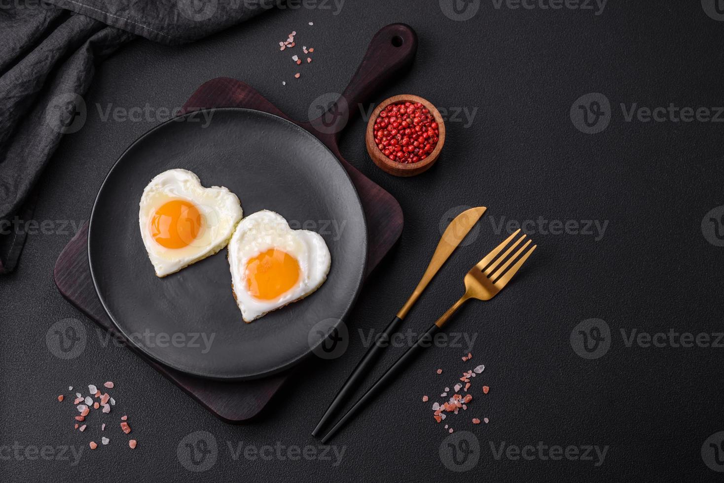 två hjärtformade friterad ägg på en svart keramisk tallrik på en mörk betong bakgrund foto