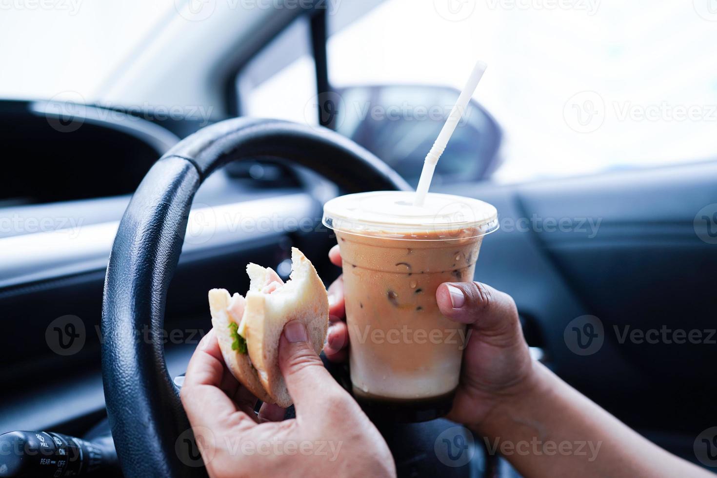 asiatisk kvinna förare håll is kaffe kopp och smörgås bröd för äta och dryck i bil, farlig och risk ett olycka. foto