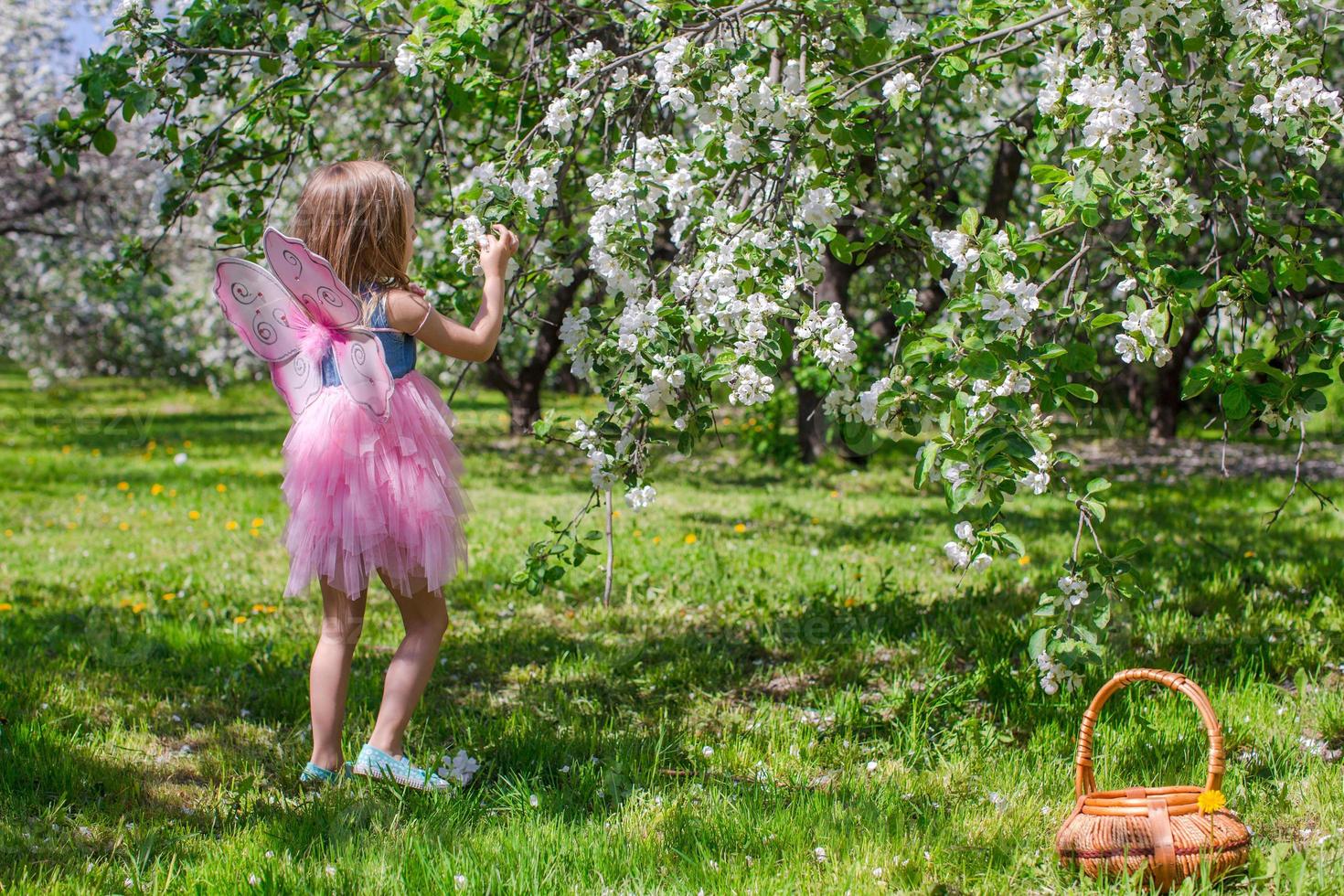 förtjusande liten flicka med sugrör korg i blomstrande äpple fruktträdgård foto