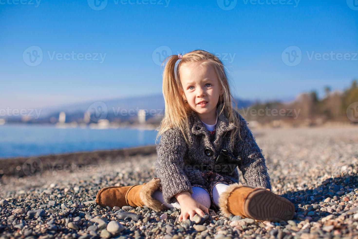 förtjusande liten flicka på de strand i en mysigt Tröja och klänning på värma vinter- dag foto