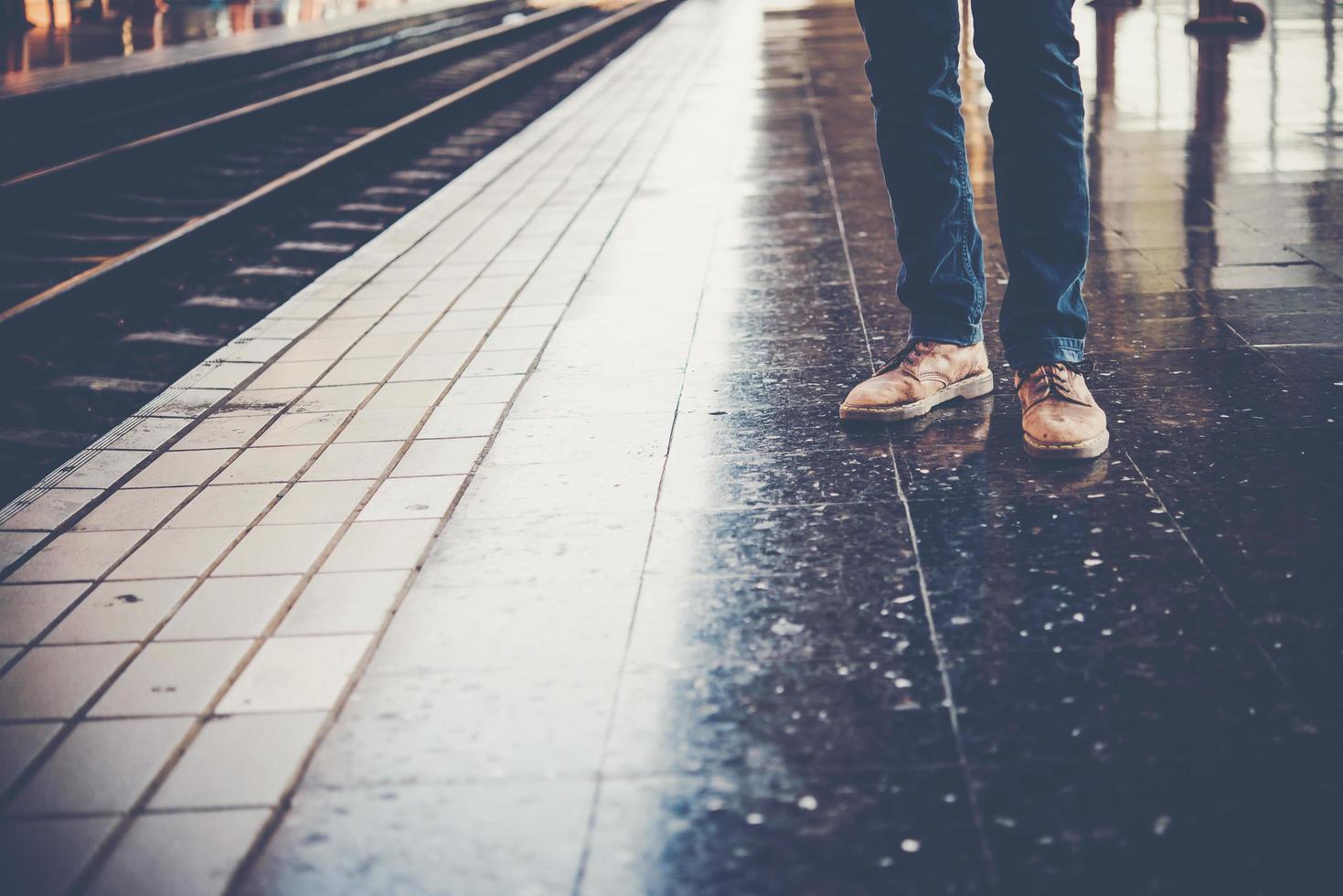 fötter på en ung man som bär jeans som väntar på tåget foto