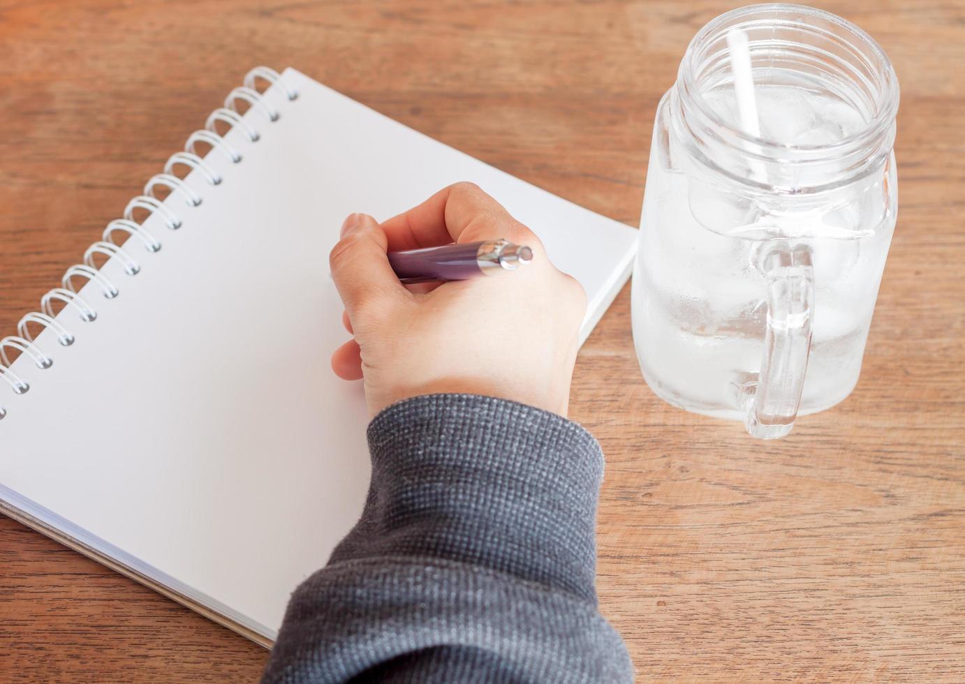 närbild av en person som skriver i en anteckningsbok med ett glas vatten foto