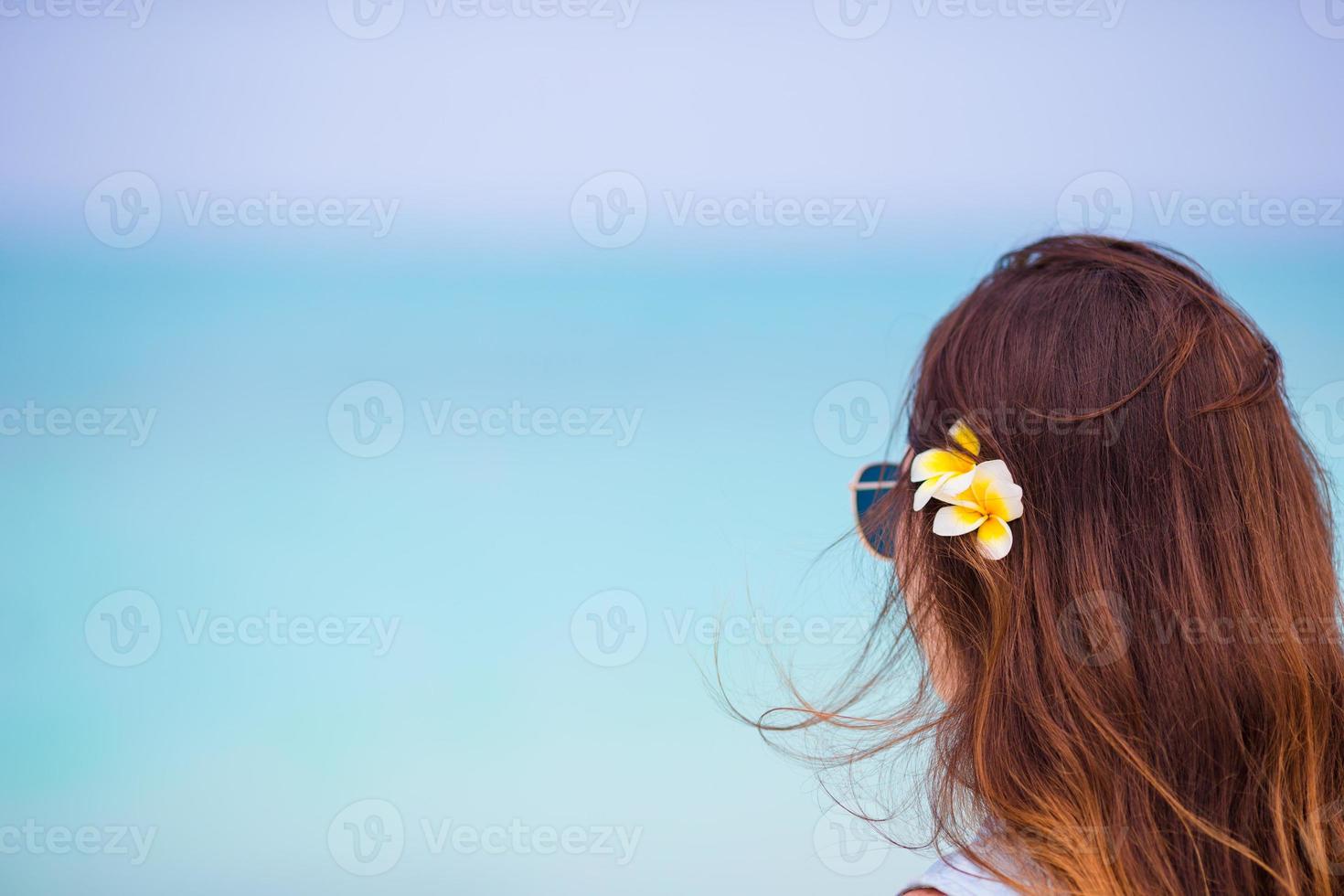 ung skön kvinna under tropisk strand semester. njut av suumer semester ensam på de strand på afrika med frangipani blommor i henne hår foto