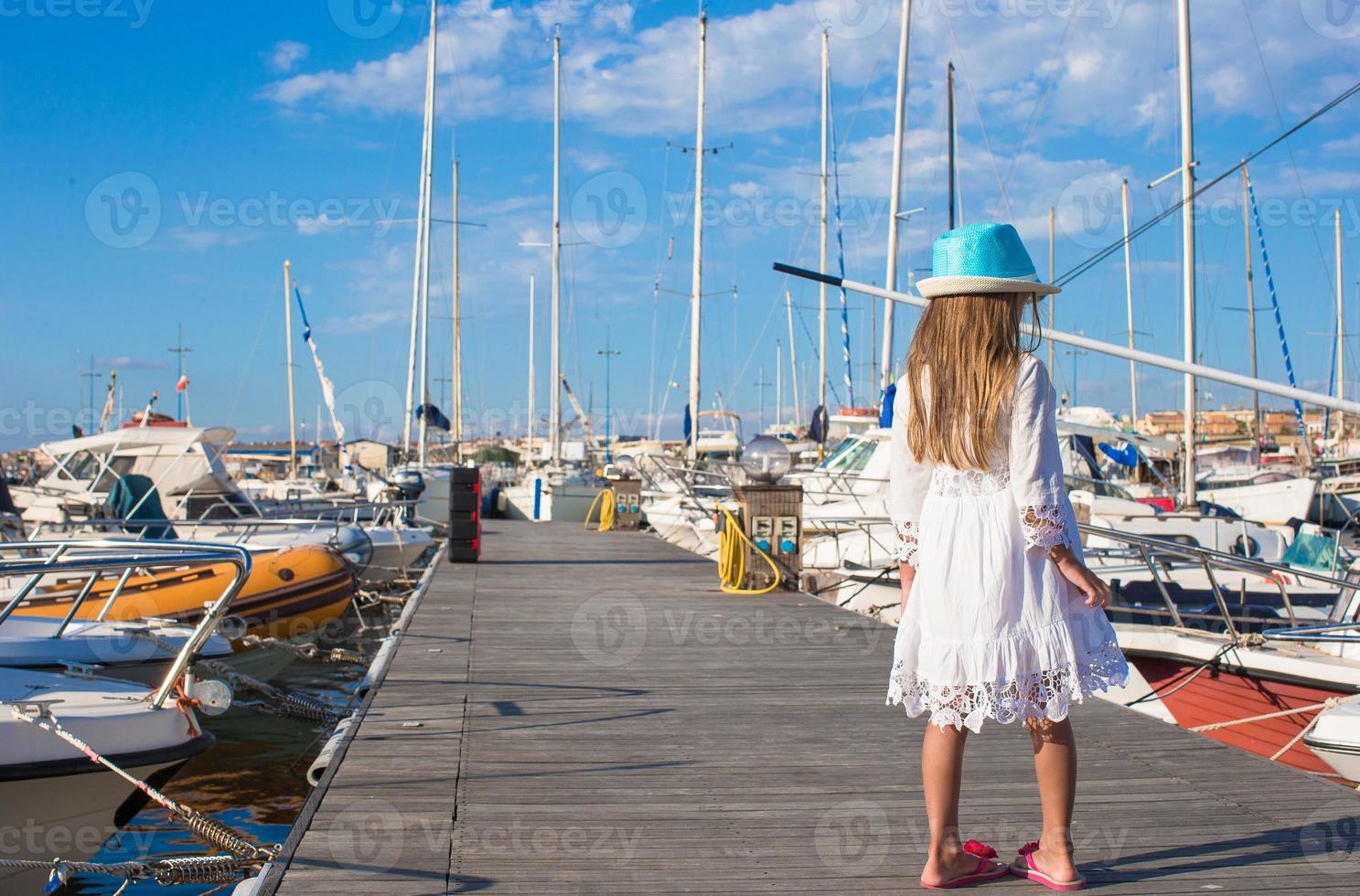 förtjusande liten flicka ha roligt i en hamn på sommar dag foto