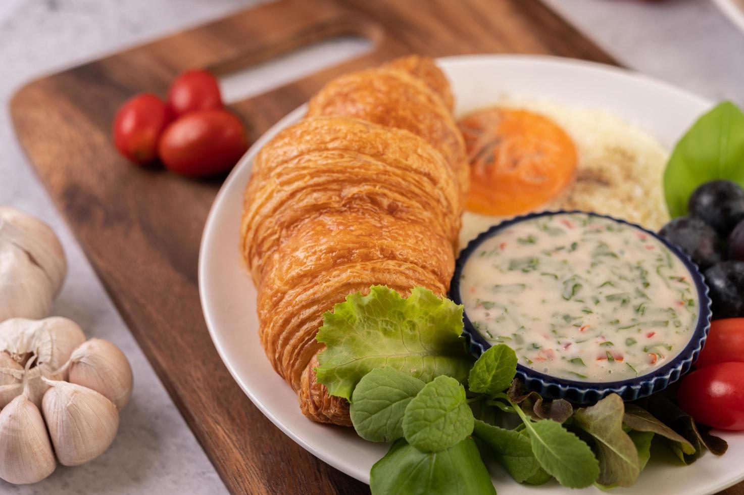 croissant, stekt ägg, salladsdressing, svarta druvor och tomater foto