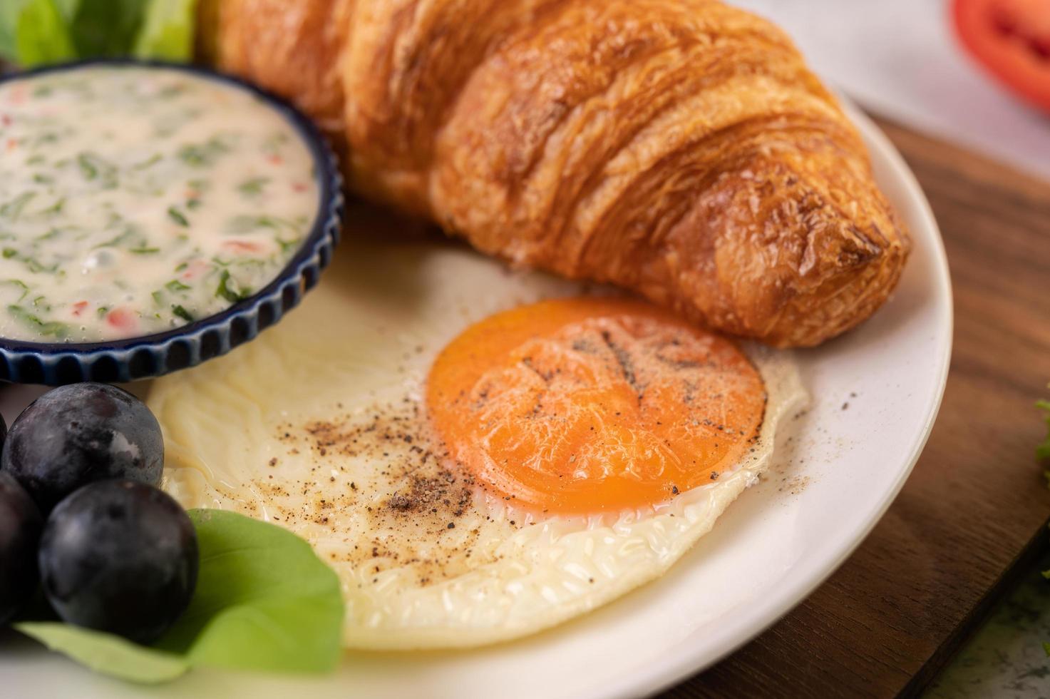 croissant, stekt ägg, salladsdressing, svarta druvor och tomater foto