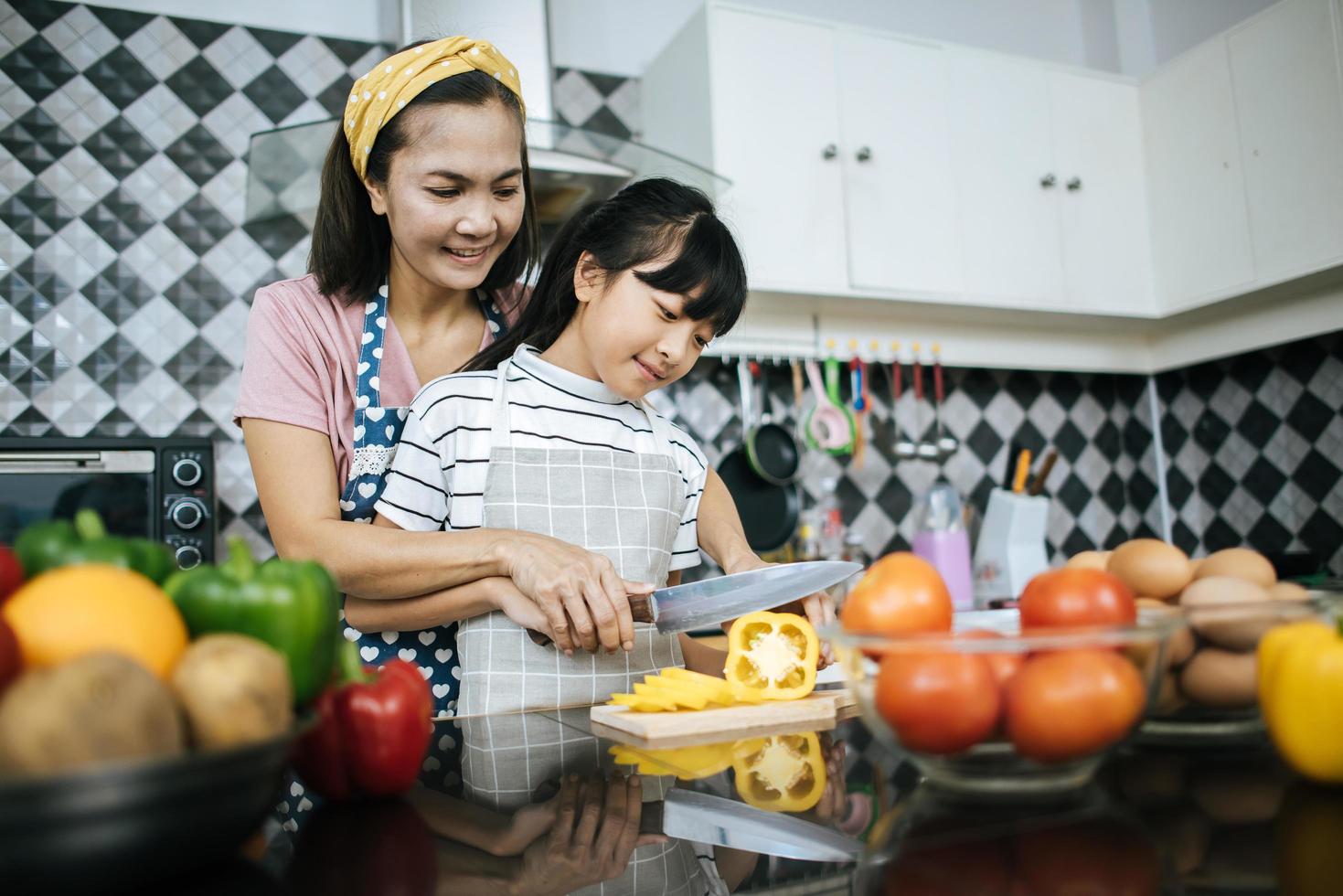 glad mamma och dotter som förbereder och hugger grönsaker i köket foto