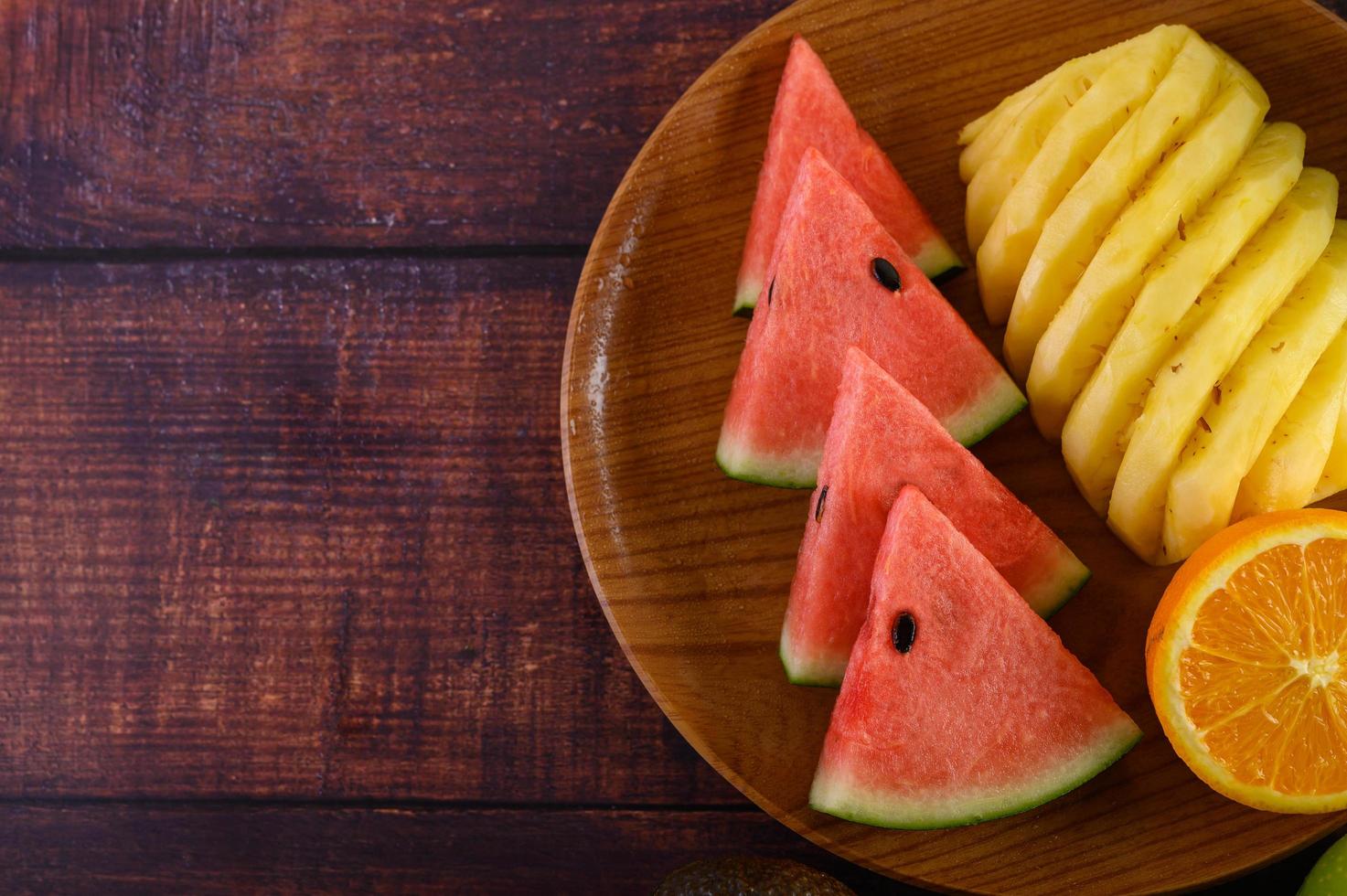 vattenmelon, apelsin och ananas skuren i bitar på en träplatta foto