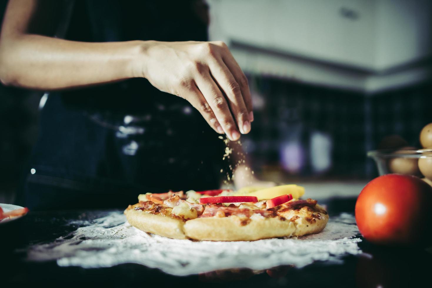 närbild av en hand som lägger oregano över en pizza foto