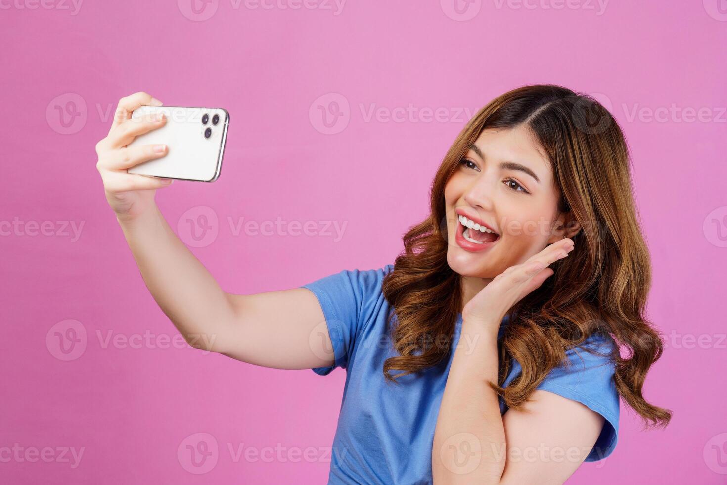 porträtt av Lycklig leende ung kvinna bär tillfällig t-shirt selfie med smartphone isolerat över rosa bakgrund foto