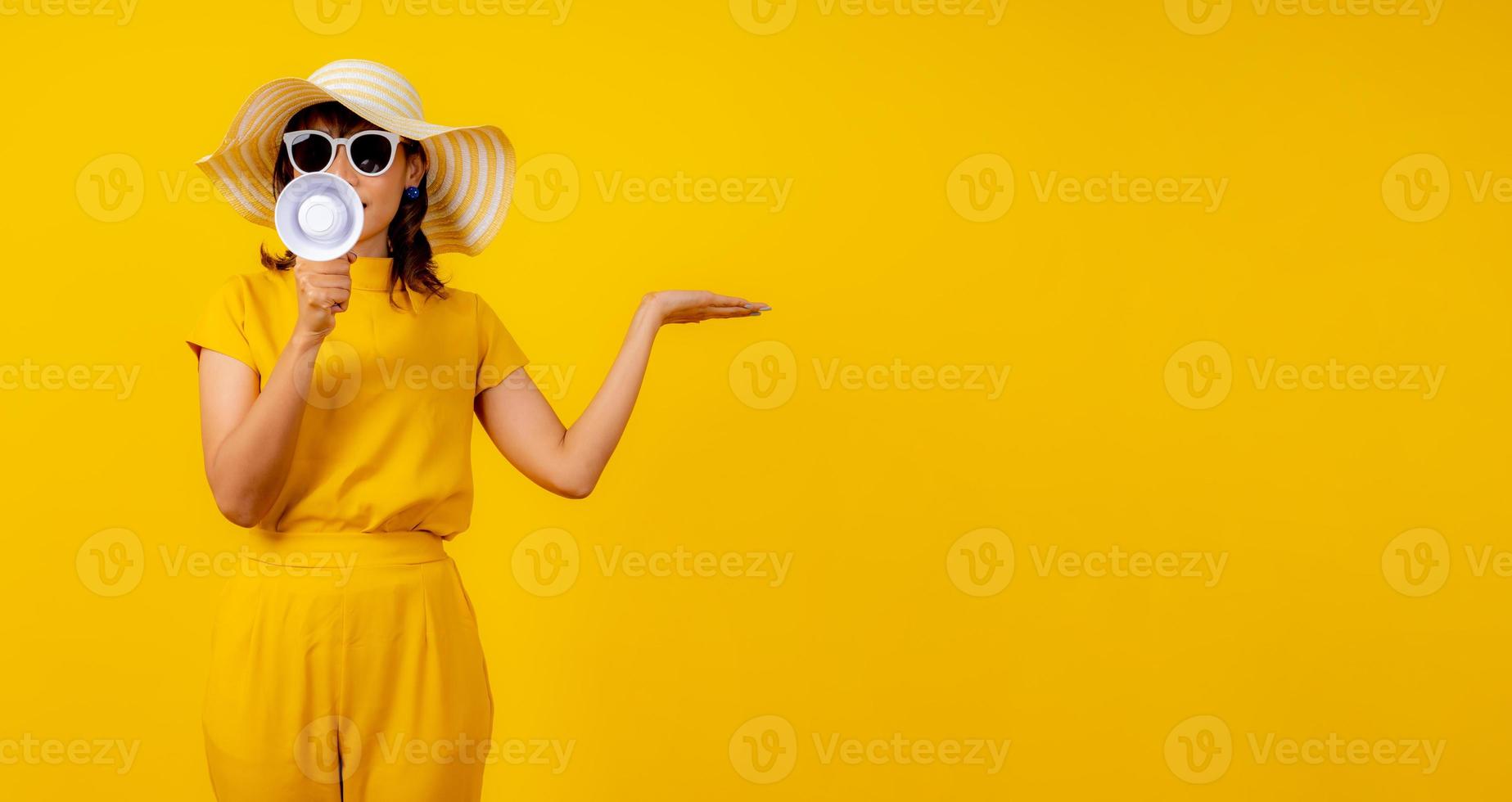 söt och rolig kvinna i gul tillfällig trasa stil och bär hatt innehav vit megafon för meddelande och visa hand till närvarande produkt foto