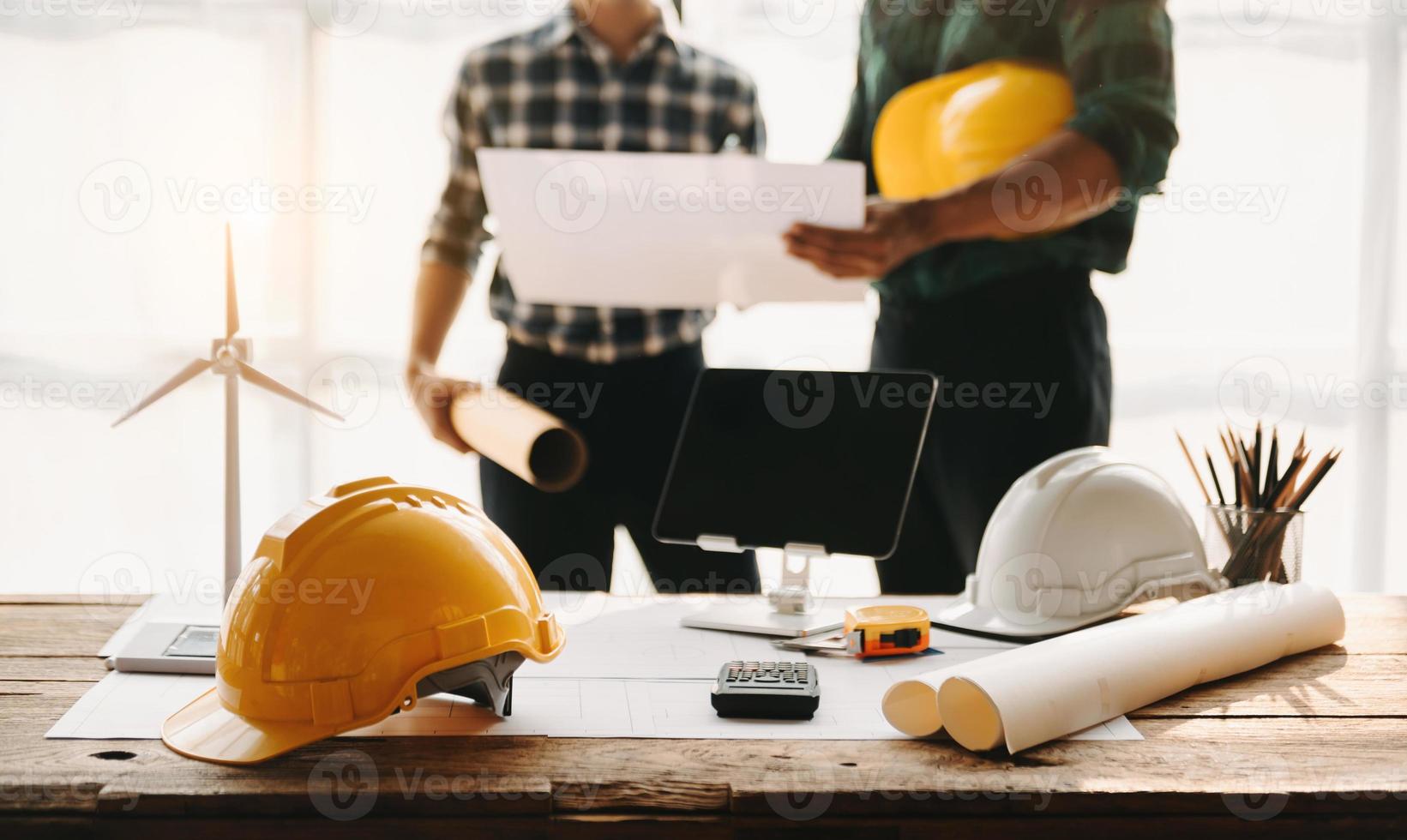 ingenjör skrivbord med objekt papper och läsplatta med suddigt ingenjör lagarbete hårt arbetande till konsulterar handla om deras byggnad projekt. foto