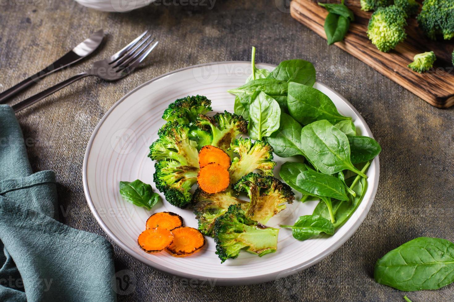 grillad broccoli och morötter och färsk spenat löv på en tallrik. vegetabiliska diet. foto