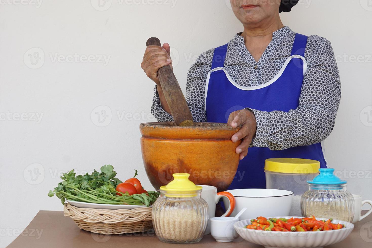 närbild senior kvinna är matlagning, ha på sig förkläde, innehar mortelstöt, murbruk. begrepp, matlagning för familj. thai kök livsstil. äldre aktivitet. foto