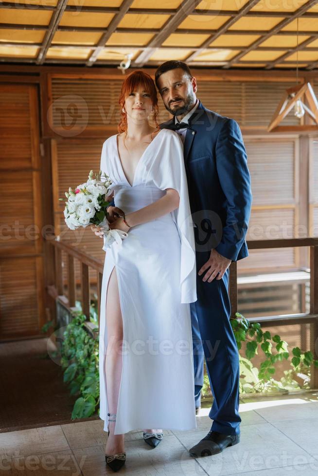 brud i en vit klänning med en bukett och de brudgum i en blå kostym foto