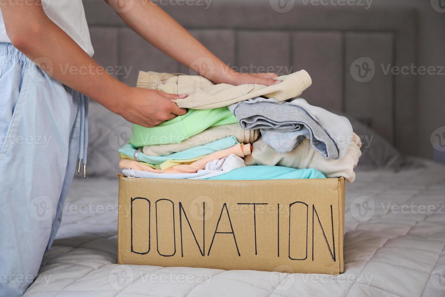 flicka sätter saker i donation låda med kläder. foto