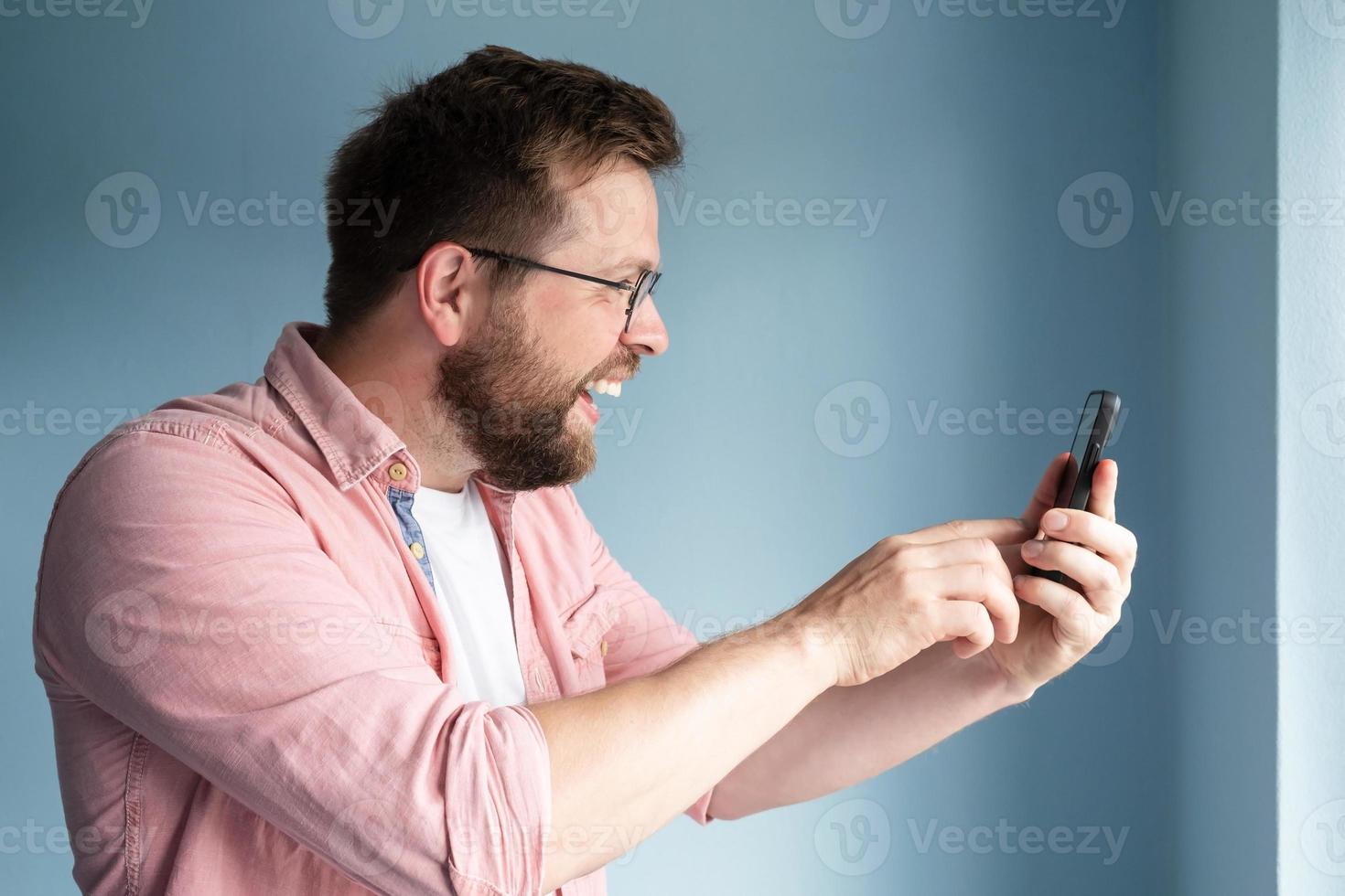 profil av en glad leende man vem innehar en smartphone i hans händer och kommunicerar uppkopplad via video kommunikation. foto