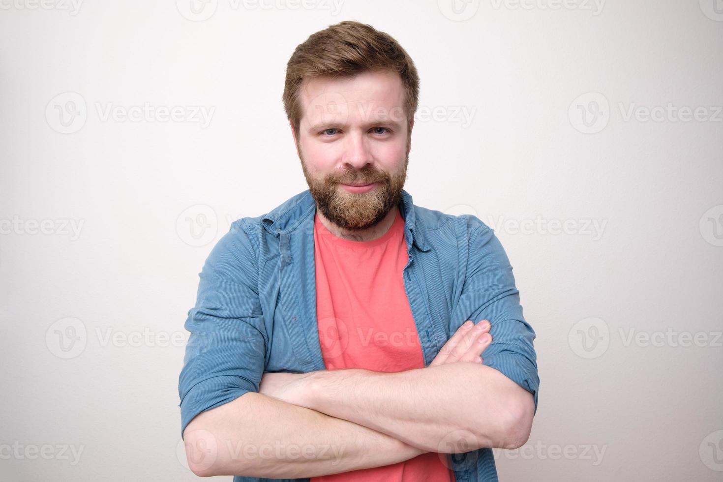 ett attraktiv caucasian man med en välvillig utseende står med korsade vapen och utseende in i de kamera. vit bakgrund. foto