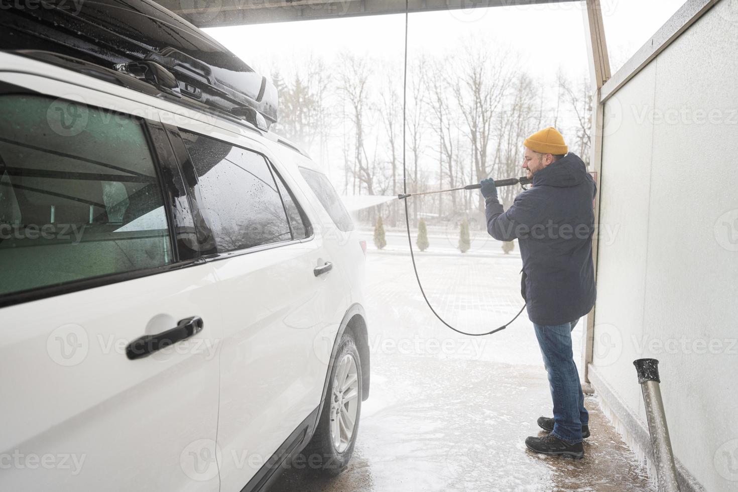 man tvättning hög tryck vatten amerikan sUV bil med tak kuggstång på själv service tvätta i kall väder. foto