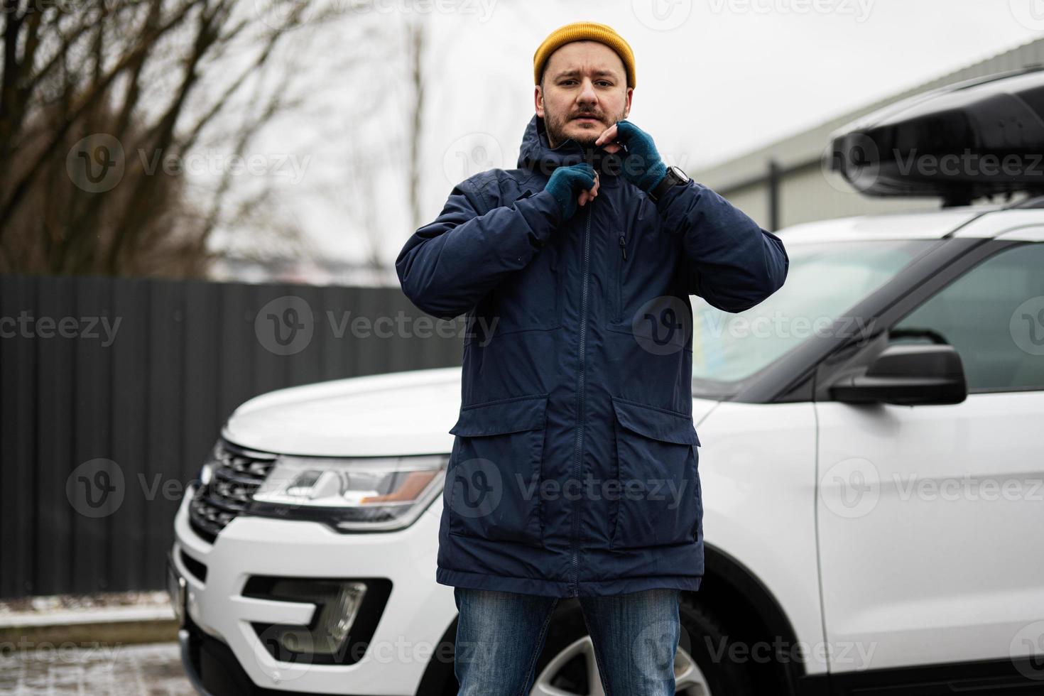 man förare ha på sig jacka och gul hatt mot hans amerikan sUV bil med tak kuggstång i kall väder. foto