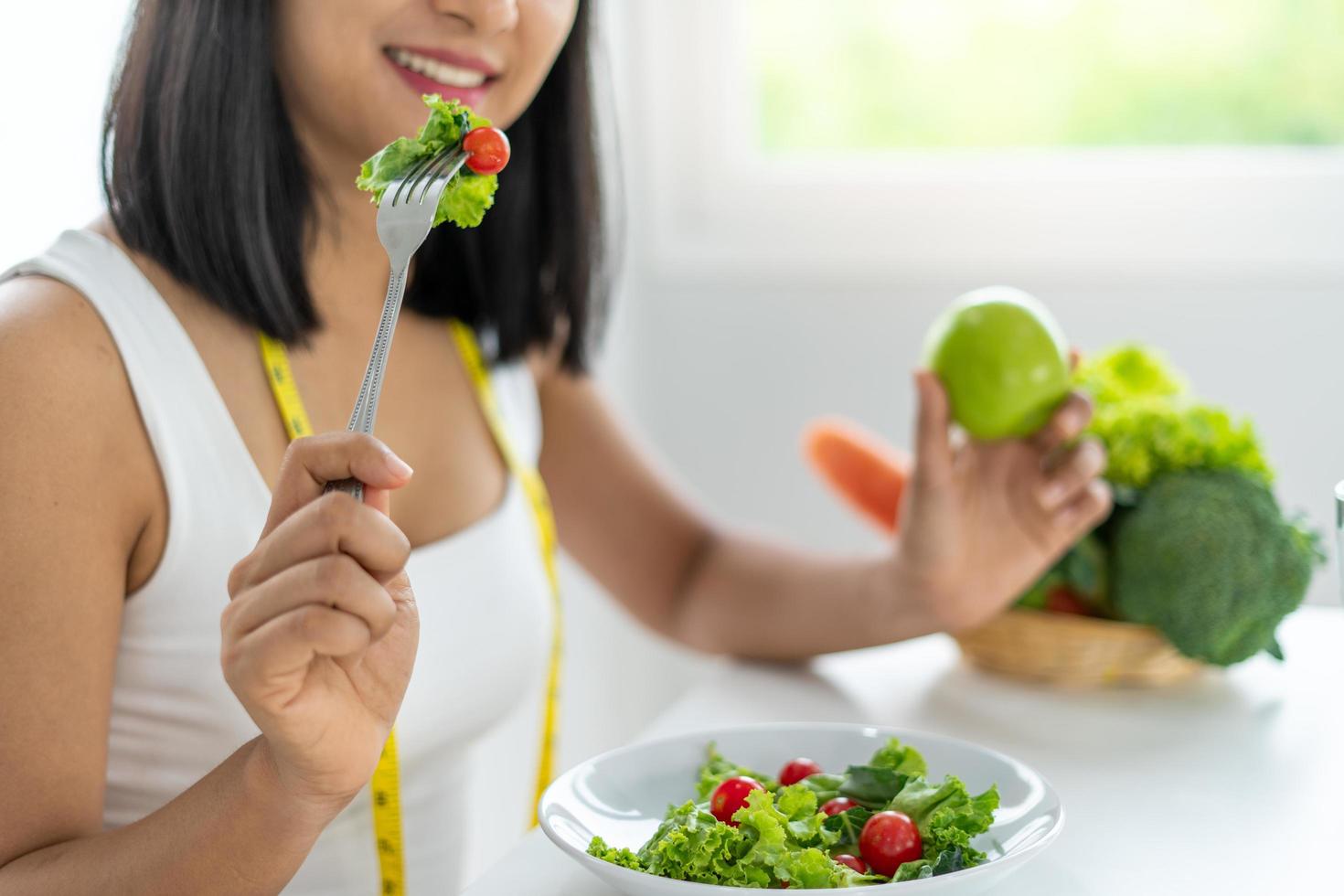 skön asiatisk kvinnor är njuter äter sallad till tappa bort vikt. friska ung kvinna äter vegetabiliska sallad. bantning , friska mat begrepp. foto